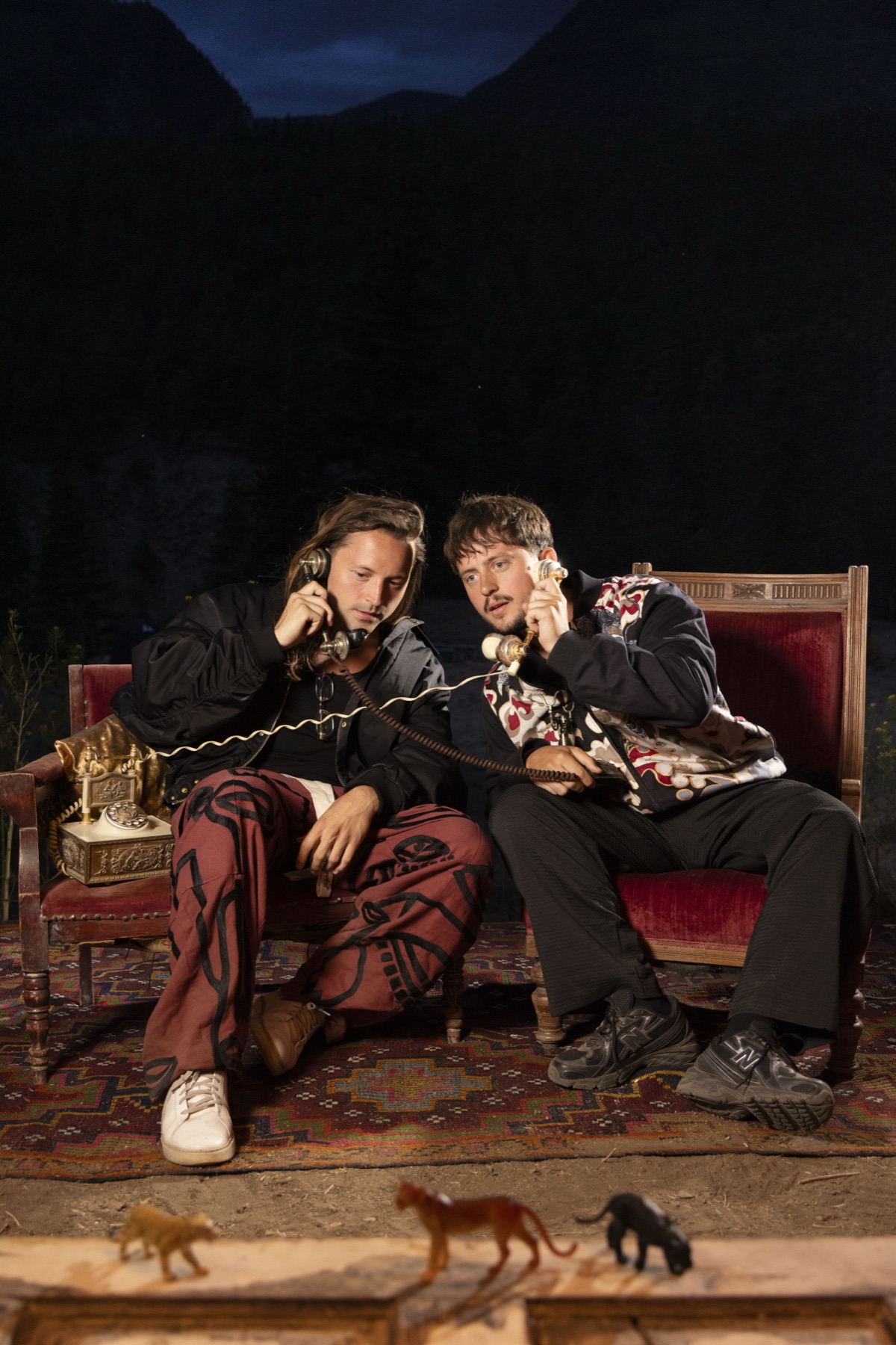 SOMMERS seated on red chairs with vintage telephones against dark mountains.